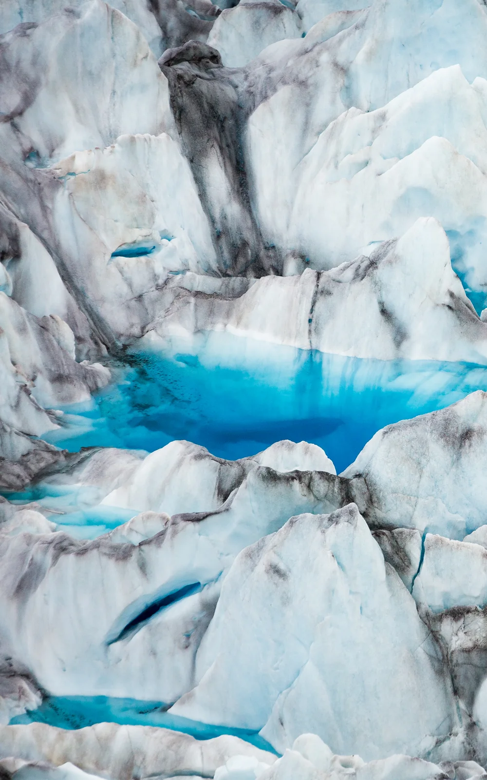 Turquoise meltwater pool surrounded by sculptural glacier formations in Alaska